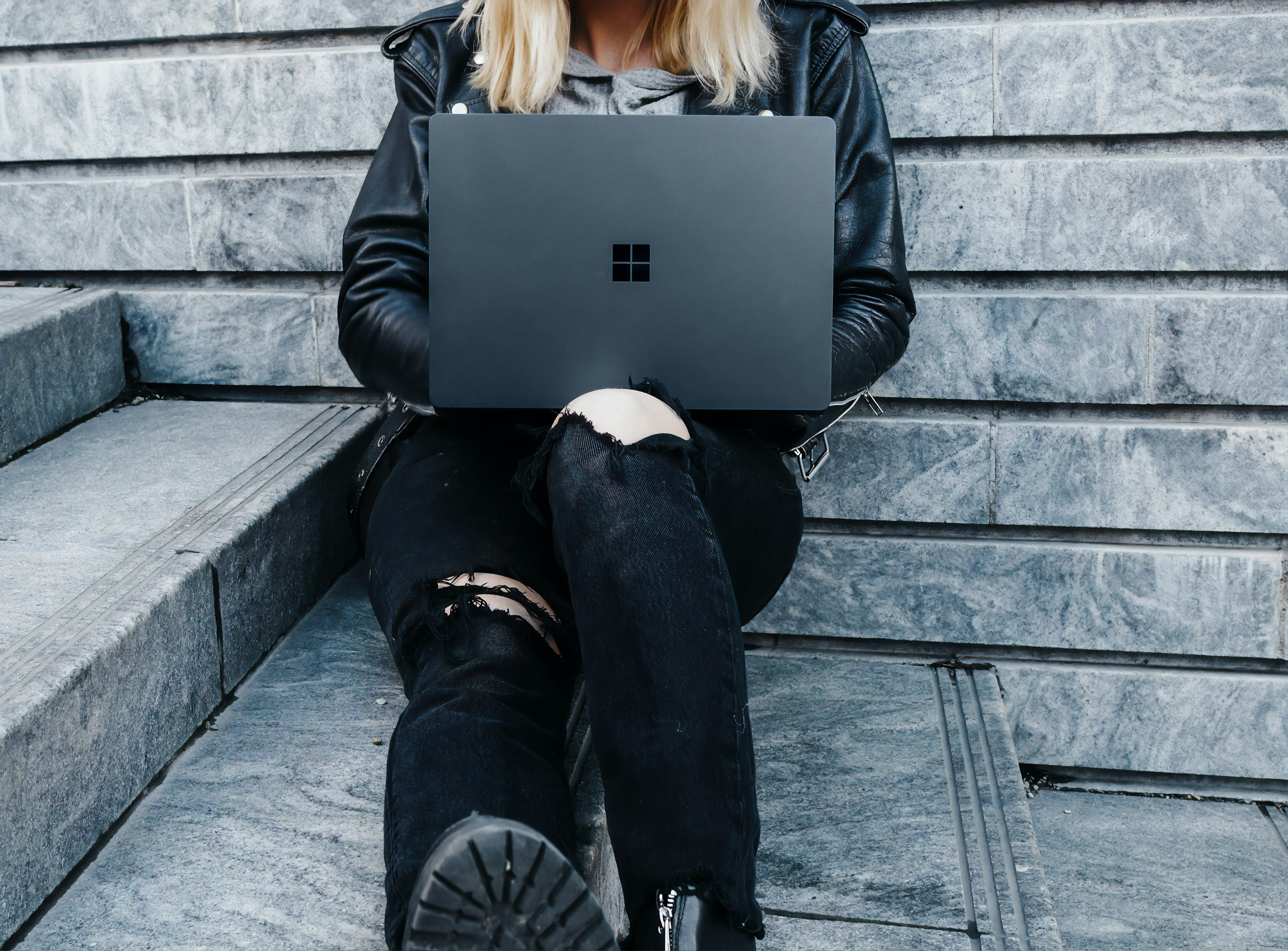 femme habillée en noir assise sur les marches avec un ordinateur